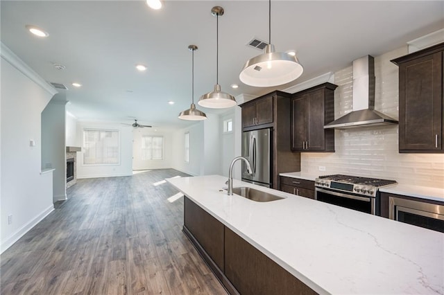 kitchen with pendant lighting, sink, backsplash, stainless steel appliances, and wall chimney range hood