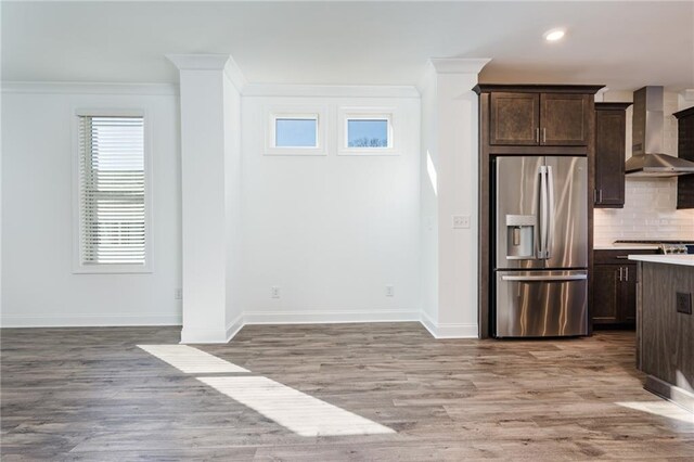 kitchen featuring tasteful backsplash, dark brown cabinets, light hardwood / wood-style flooring, stainless steel fridge, and wall chimney range hood