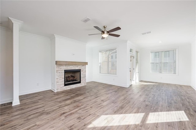 unfurnished living room with hardwood / wood-style flooring, a stone fireplace, ornamental molding, and ceiling fan