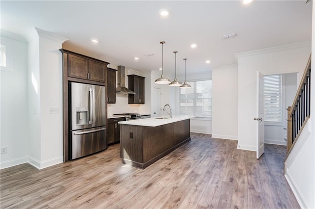 kitchen featuring sink, decorative light fixtures, an island with sink, stainless steel appliances, and wall chimney range hood