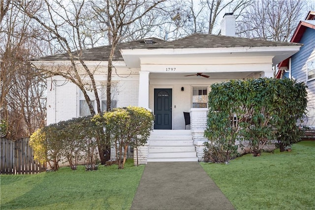 view of exterior entry with ceiling fan, covered porch, and a lawn