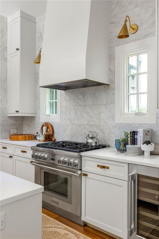 kitchen featuring custom exhaust hood, light hardwood / wood-style flooring, white cabinets, beverage cooler, and high end stainless steel range