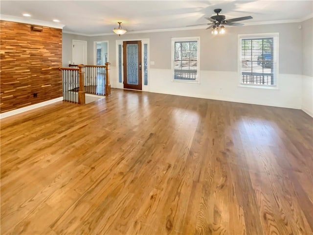 unfurnished living room with crown molding, wooden walls, and wood finished floors