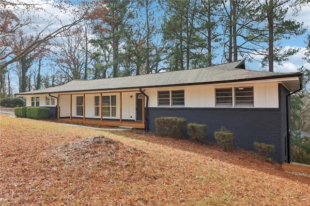 ranch-style house featuring covered porch, brick siding, and roof with shingles