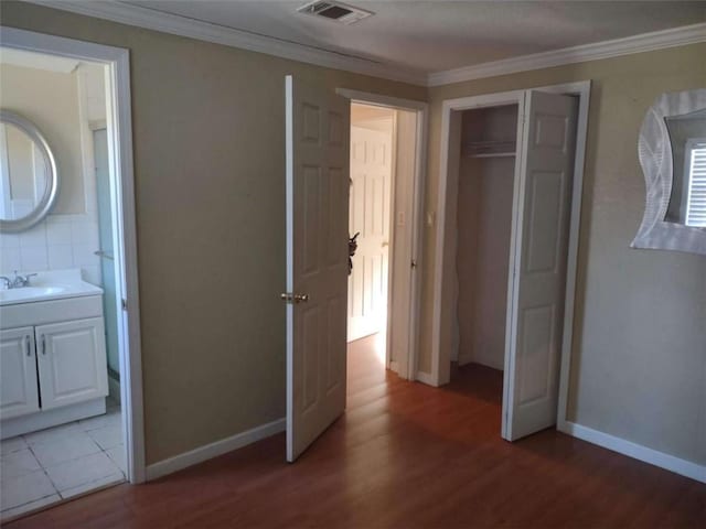 unfurnished bedroom featuring hardwood / wood-style flooring, sink, crown molding, and connected bathroom