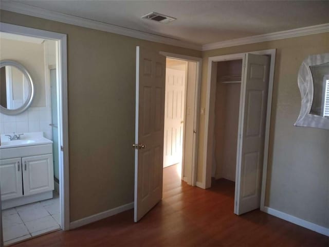 unfurnished bedroom featuring crown molding, light wood-type flooring, sink, and connected bathroom