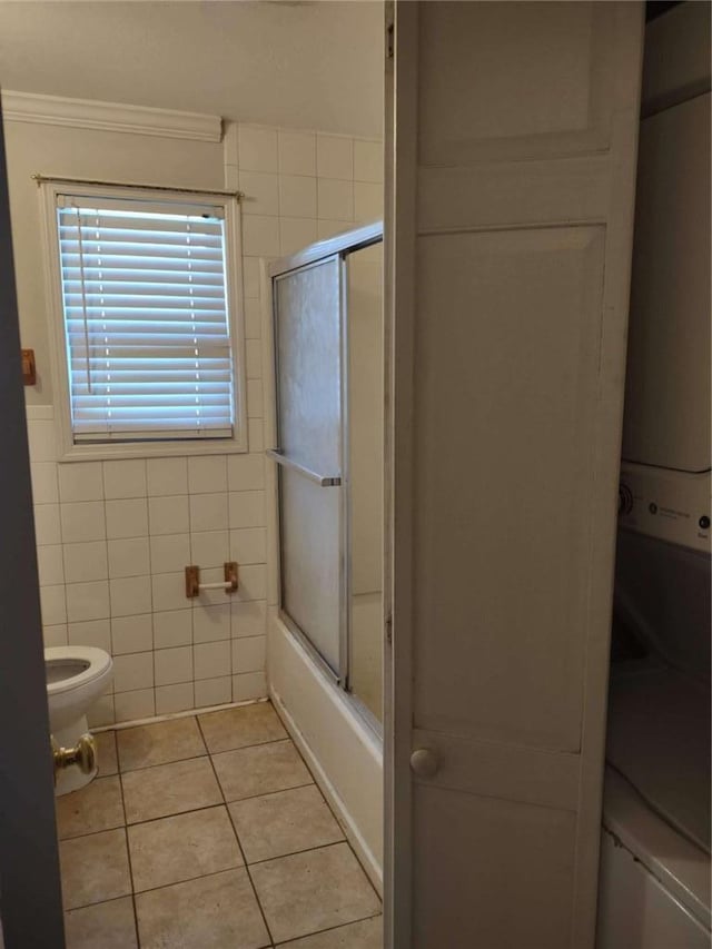 bathroom with tile patterned flooring, crown molding, combined bath / shower with glass door, toilet, and tile walls