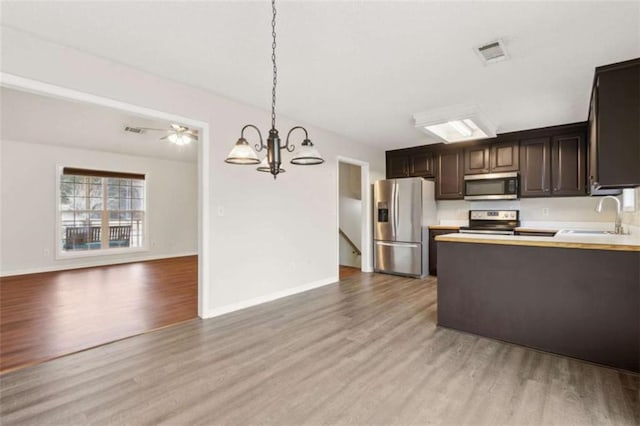 kitchen with decorative light fixtures, sink, light wood-type flooring, and appliances with stainless steel finishes