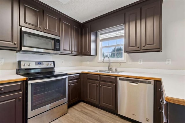 kitchen with sink, dark brown cabinetry, appliances with stainless steel finishes, and light hardwood / wood-style flooring