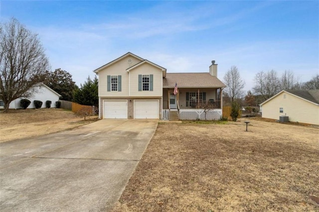 split level home featuring covered porch, cooling unit, a front yard, and a garage