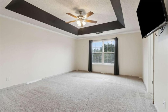 empty room featuring light carpet, ceiling fan, a tray ceiling, a textured ceiling, and ornamental molding