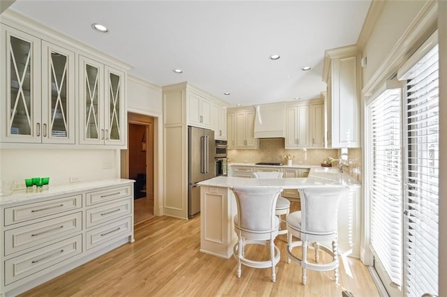 kitchen featuring appliances with stainless steel finishes, a breakfast bar, backsplash, light hardwood / wood-style floors, and kitchen peninsula