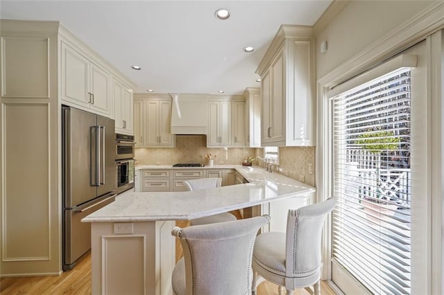 kitchen featuring appliances with stainless steel finishes, a kitchen bar, custom exhaust hood, kitchen peninsula, and cream cabinets