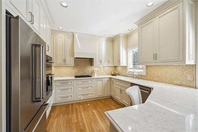 kitchen featuring appliances with stainless steel finishes, sink, light stone countertops, custom range hood, and light wood-type flooring