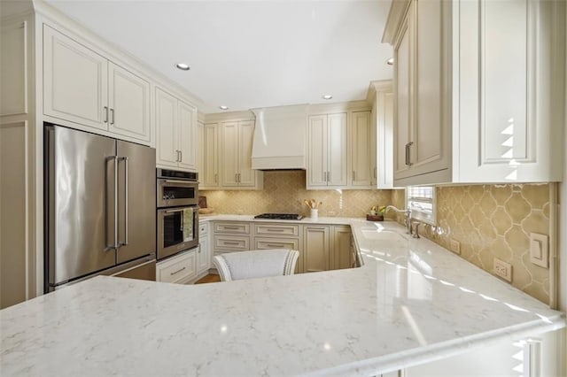 kitchen with stainless steel appliances, premium range hood, tasteful backsplash, and light stone counters