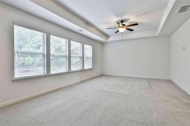 carpeted empty room with ceiling fan and a raised ceiling