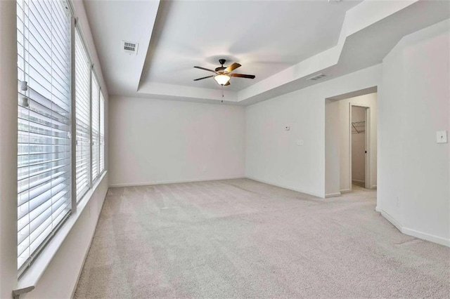 unfurnished room featuring visible vents, baseboards, light colored carpet, a tray ceiling, and a ceiling fan