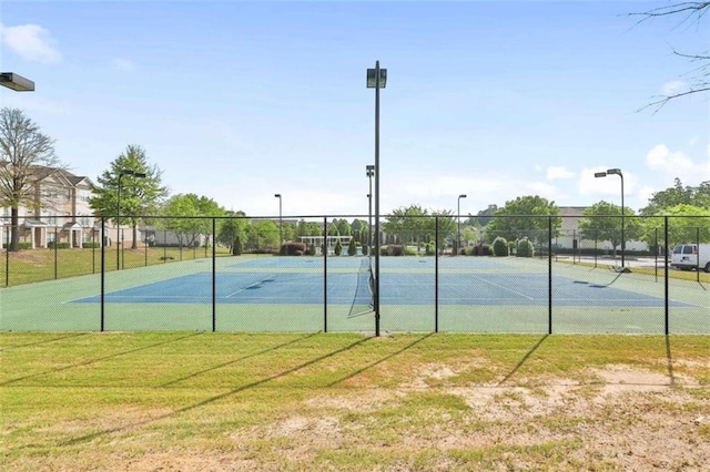 view of tennis court with a lawn and fence