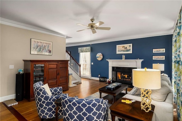 living room with a glass covered fireplace, stairway, wood finished floors, and crown molding