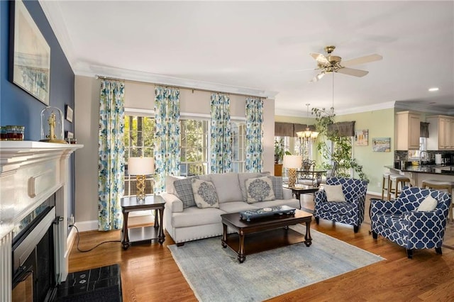 living room with a fireplace with flush hearth, crown molding, wood finished floors, and ceiling fan with notable chandelier