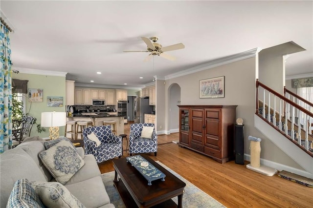 living room with stairway, arched walkways, light wood finished floors, and ornamental molding