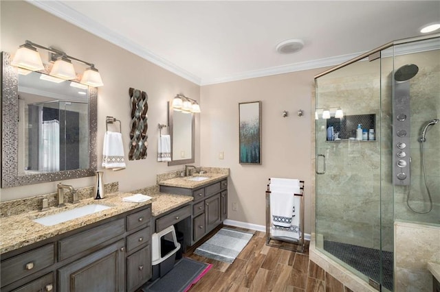 bathroom with crown molding, double vanity, a stall shower, a sink, and wood finished floors