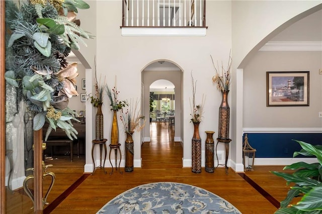 entryway featuring arched walkways, wood finished floors, a towering ceiling, baseboards, and ornamental molding