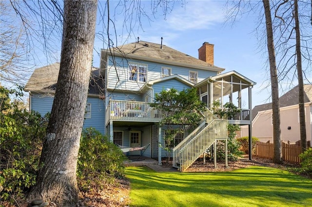 back of house featuring a deck, fence, a sunroom, stairs, and a lawn