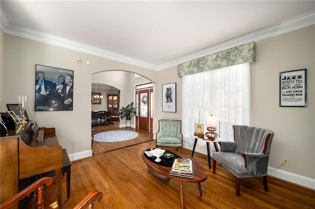 sitting room with baseboards, crown molding, arched walkways, and wood finished floors