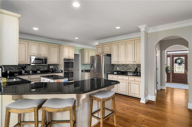 kitchen with arched walkways, appliances with stainless steel finishes, a kitchen bar, and cream cabinetry