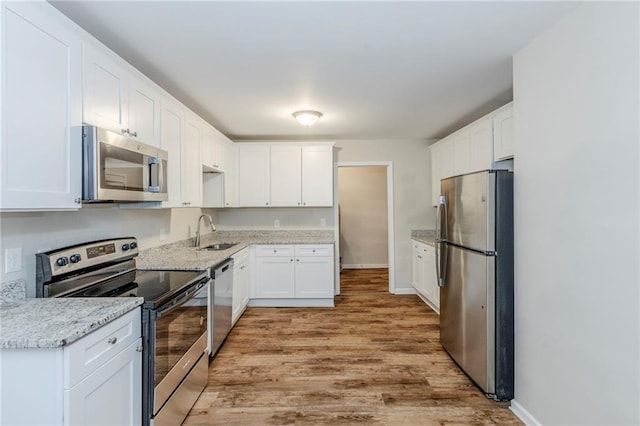 kitchen with stainless steel appliances, a sink, white cabinetry, and light stone countertops