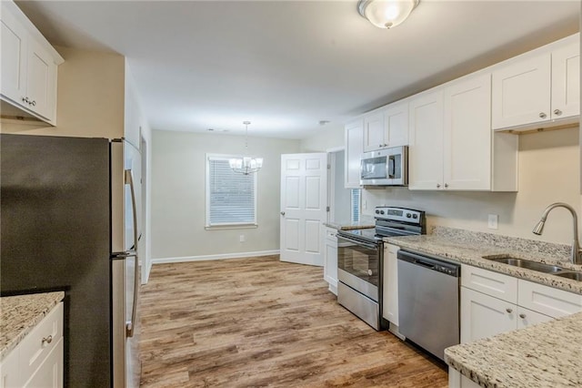 kitchen featuring light wood-style flooring, appliances with stainless steel finishes, a sink, white cabinetry, and a notable chandelier