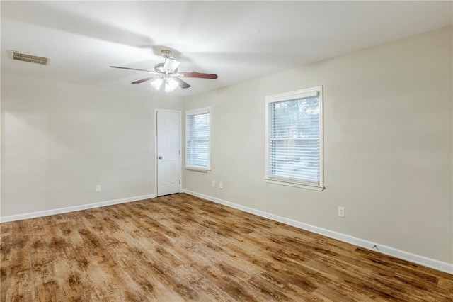 empty room with a ceiling fan, wood finished floors, visible vents, and baseboards