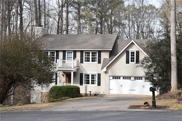 colonial house with an attached garage, a balcony, a shingled roof, driveway, and a chimney