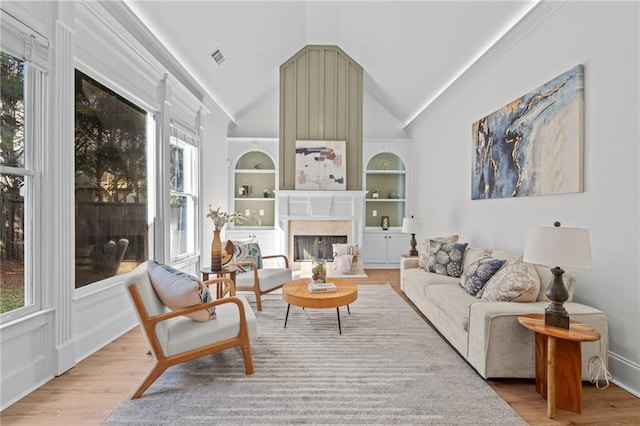 living room featuring light wood finished floors, built in shelves, vaulted ceiling, and a fireplace
