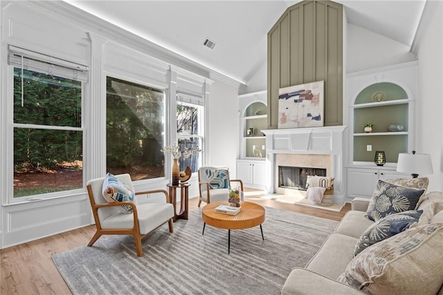 living room featuring a high end fireplace, built in features, wood finished floors, and lofted ceiling