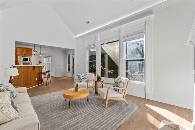 living room with visible vents, light wood-style flooring, a healthy amount of sunlight, and high vaulted ceiling