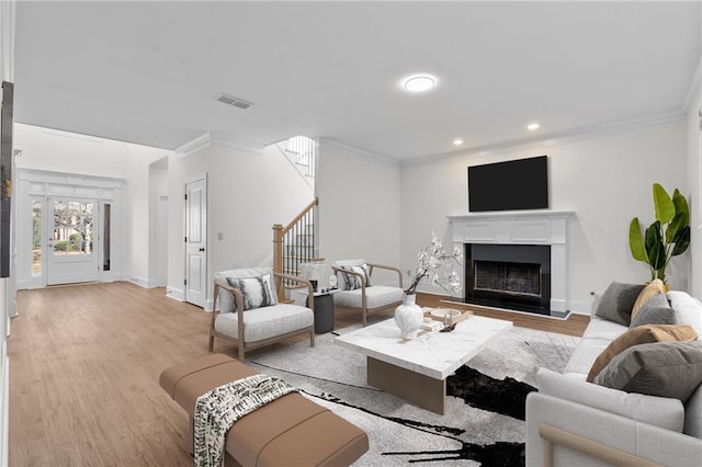 living room with visible vents, ornamental molding, stairway, and light wood-type flooring