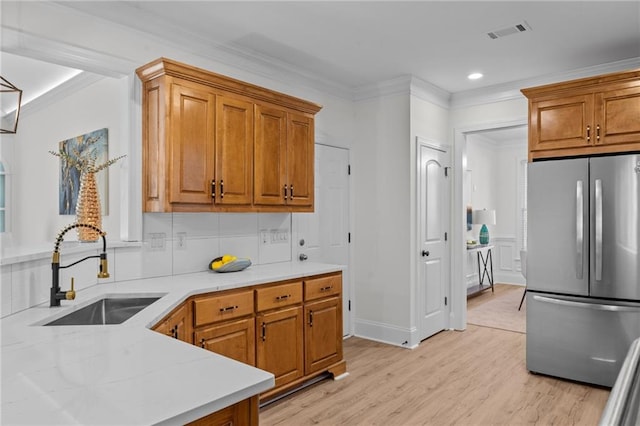 kitchen with freestanding refrigerator, brown cabinets, a sink, and light countertops