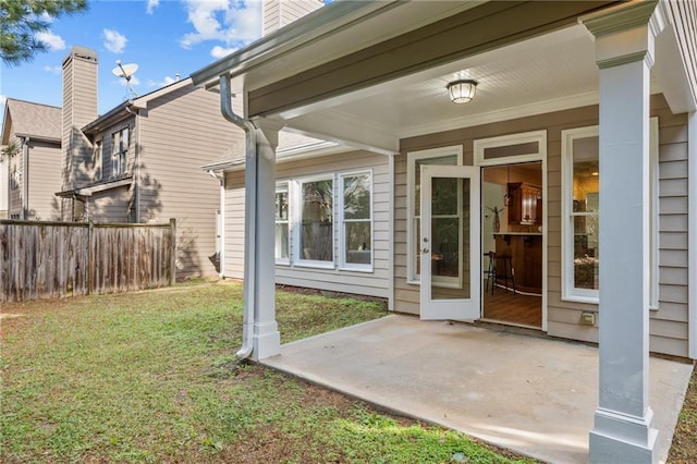 view of exterior entry with a yard, fence, a chimney, and a patio area