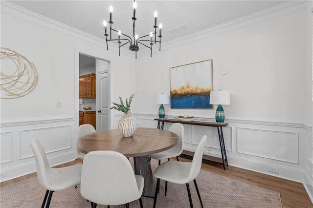 dining room with wainscoting, a chandelier, ornamental molding, and wood finished floors
