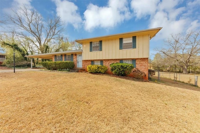split level home with a front lawn, fence, board and batten siding, an attached carport, and brick siding