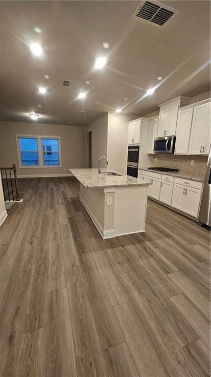 kitchen featuring white cabinetry, sink, light stone counters, dark hardwood / wood-style floors, and a center island with sink