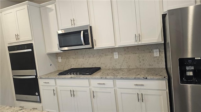 kitchen with backsplash, light stone countertops, white cabinets, and stainless steel appliances