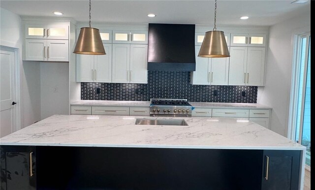 kitchen with wall chimney exhaust hood, tasteful backsplash, high end stove, and a center island with sink