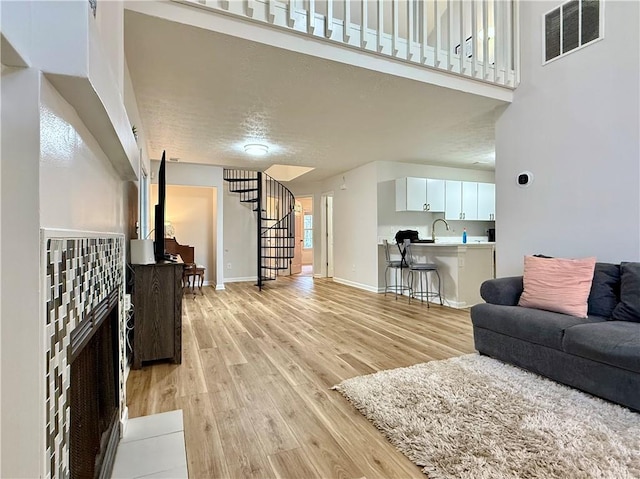 living room with visible vents, stairway, light wood-style floors, a high ceiling, and baseboards