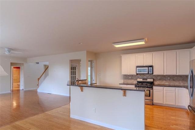 851 Roget Ct, Lawrenceville, GA 30045 - kitchen featuring stainless steel appliances, light wood-style flooring, dark countertops, backsplash, and white cabinetry