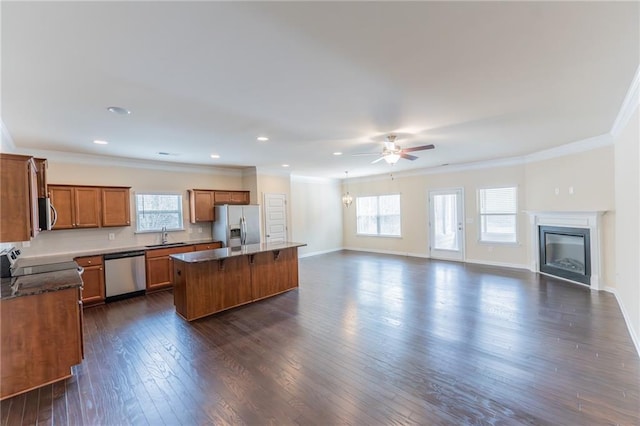 kitchen featuring stainless steel appliances, open floor plan, ornamental molding, brown cabinets, and dark wood-style floors