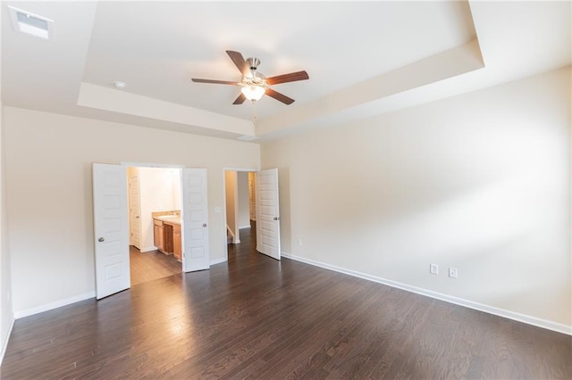 unfurnished bedroom featuring ceiling fan, dark wood-type flooring, visible vents, baseboards, and a raised ceiling