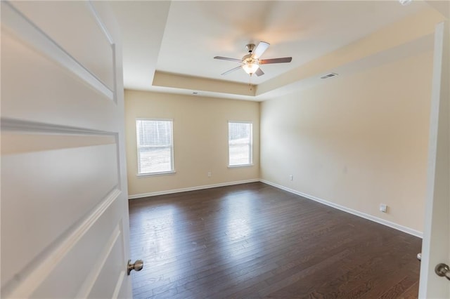 empty room with baseboards, visible vents, a tray ceiling, and dark wood-type flooring